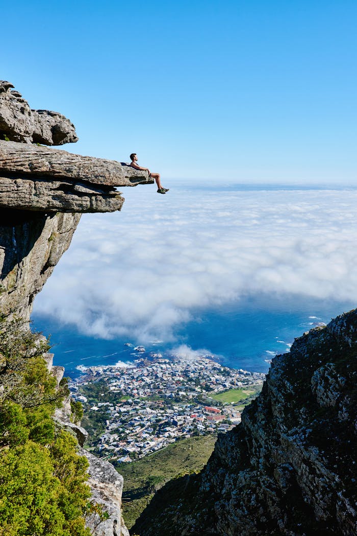 A person sits on a cliff edge enjoying a breathtaking view of the ocean and city below.